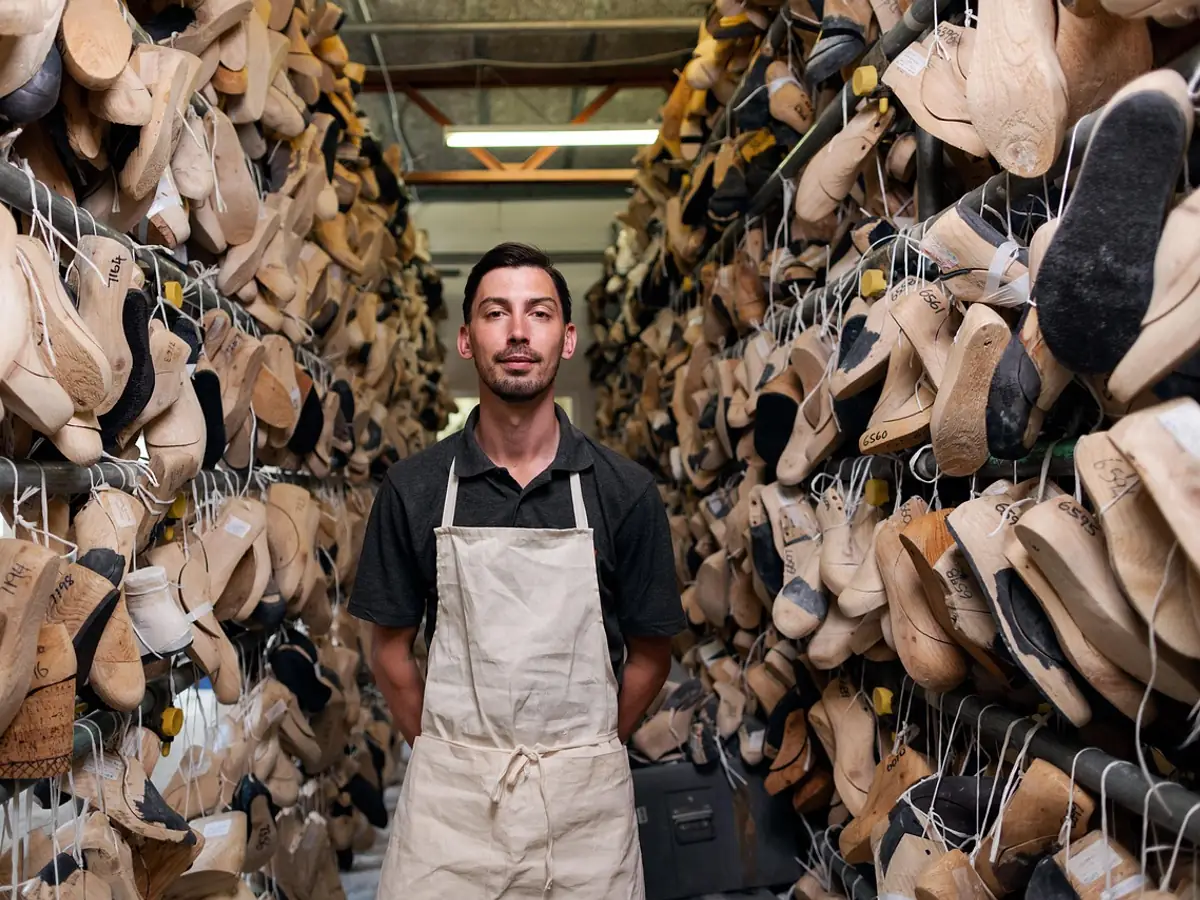 A shoemaker standing between racks of stock in his workshop